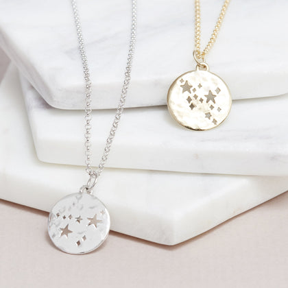 silver hammered constellation disc charm on silver belcher chain necklace laying next to a gold hammered constellation disc charm on a gold belcher chain necklace.